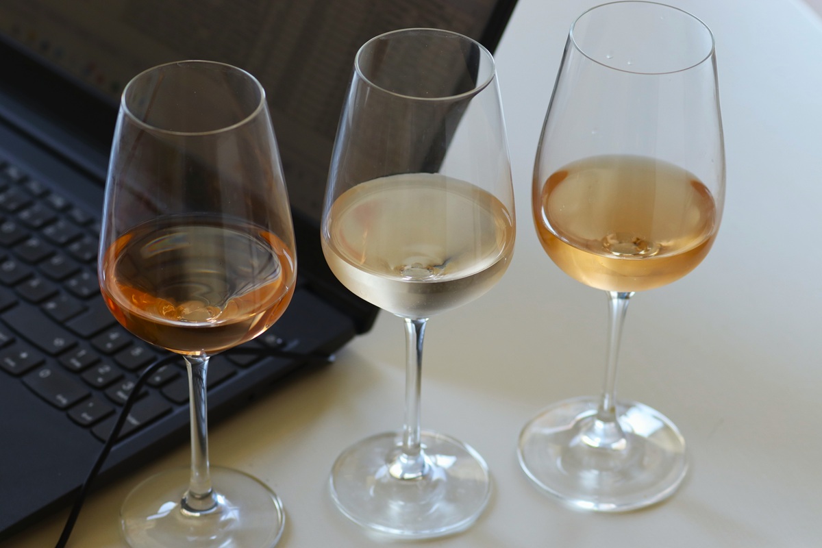 Auf dem Bild sind drei Gläser mit unterschiedlichen gefärbtem Roséwein im Vordergrund und einem Laptop im Hintergrund